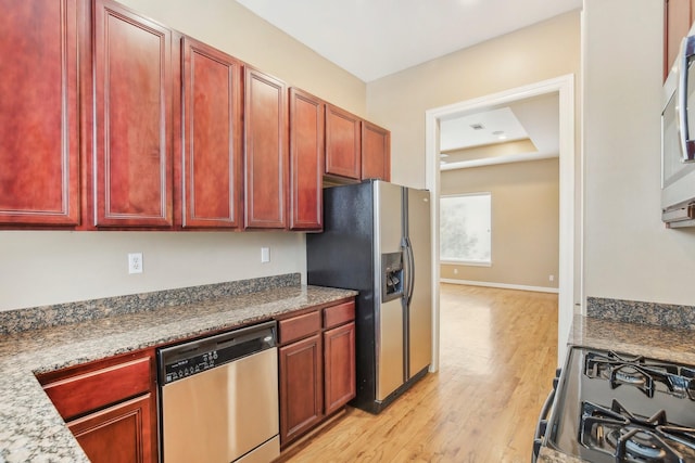 kitchen featuring light wood finished floors, baseboards, a tray ceiling, stainless steel appliances, and reddish brown cabinets