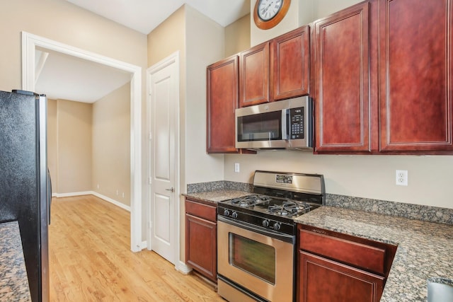 kitchen featuring dark stone countertops, baseboards, stainless steel appliances, dark brown cabinets, and light wood-style floors