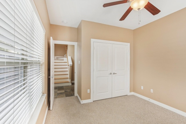 unfurnished bedroom featuring a closet, light carpet, baseboards, and ceiling fan