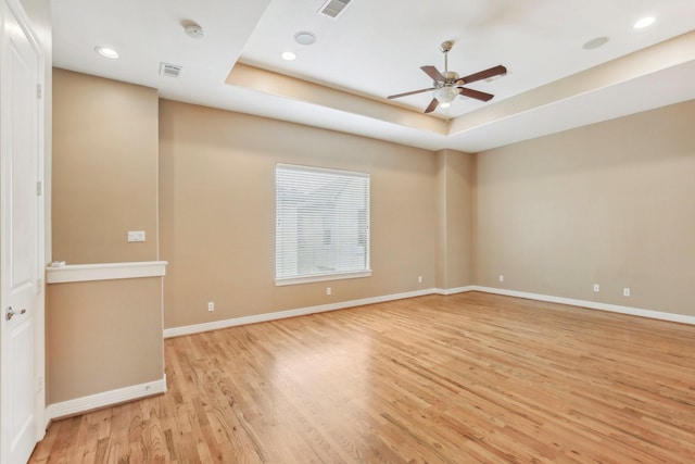 unfurnished room with ceiling fan, a tray ceiling, visible vents, and light wood-style flooring