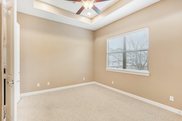 empty room with ceiling fan, a tray ceiling, baseboards, and carpet floors