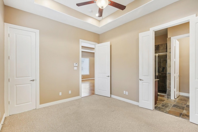 unfurnished bedroom featuring a tray ceiling, baseboards, carpet, and ensuite bathroom