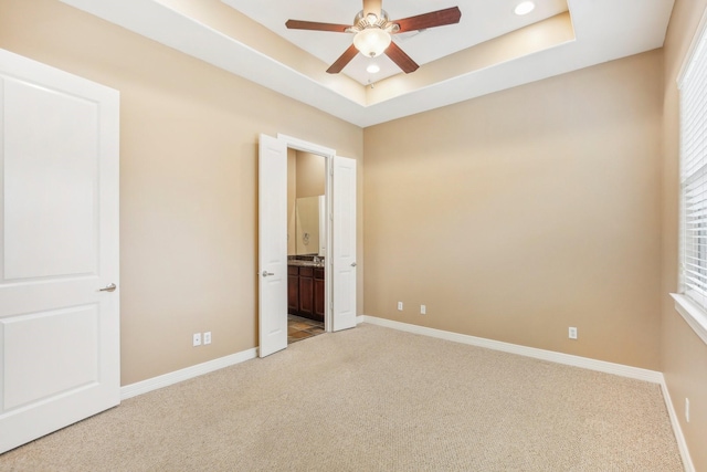 unfurnished bedroom featuring a raised ceiling, recessed lighting, connected bathroom, baseboards, and light colored carpet