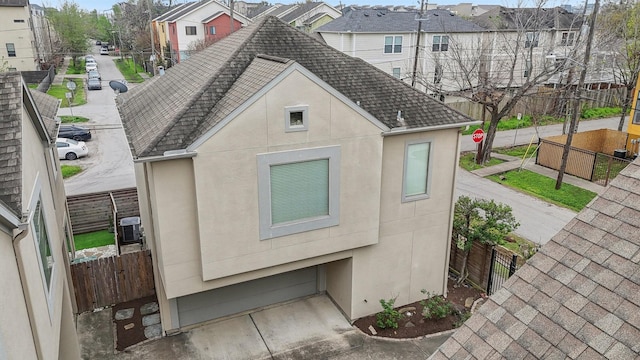 exterior space featuring stucco siding, a shingled roof, and fence