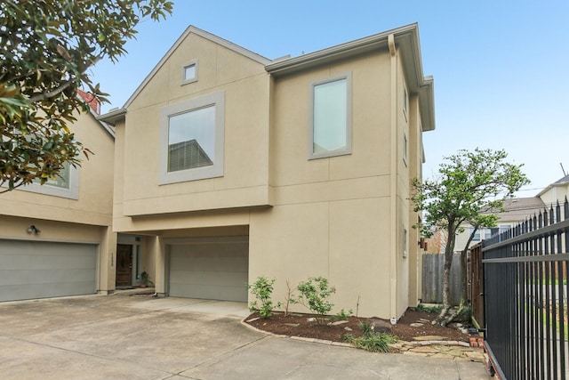 view of front of home featuring fence, a garage, driveway, and stucco siding