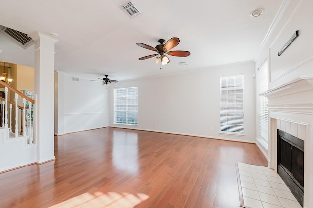 unfurnished living room with visible vents, stairs, light wood-style flooring, a fireplace, and a ceiling fan