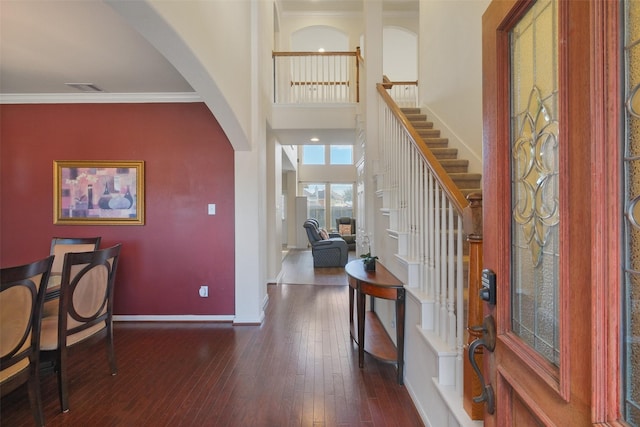 foyer entrance with baseboards, arched walkways, dark wood-type flooring, a towering ceiling, and crown molding