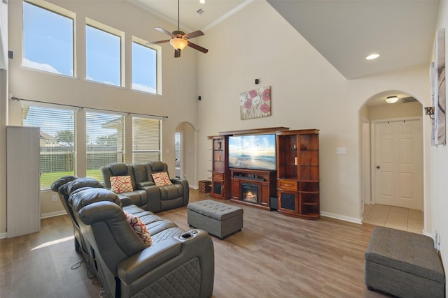 living area with arched walkways, baseboards, light wood-style floors, and a ceiling fan