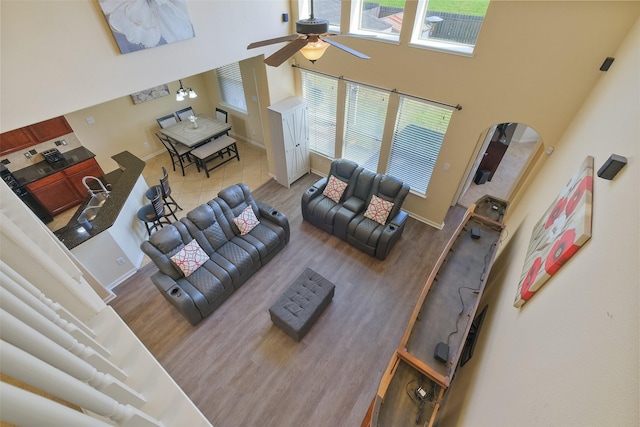 living room with wood finished floors, a ceiling fan, baseboards, a high ceiling, and arched walkways