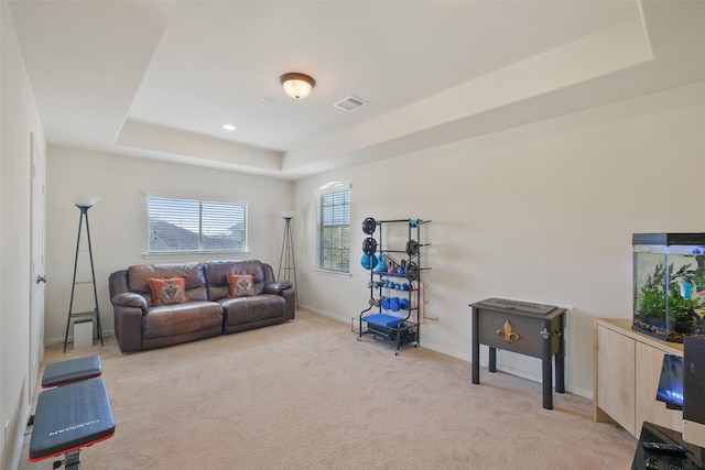 living room featuring a raised ceiling, light colored carpet, visible vents, and baseboards