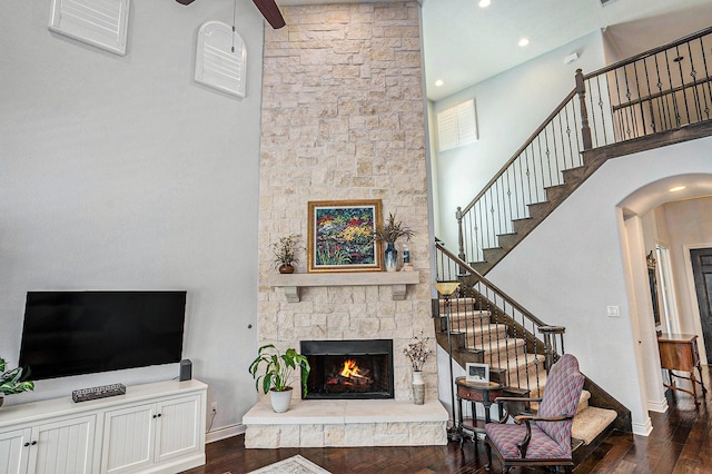 living room with a stone fireplace, stairs, a towering ceiling, and wood finished floors