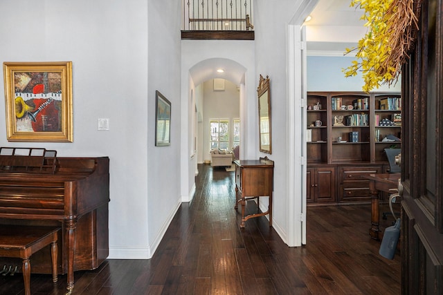 hallway with arched walkways, dark wood finished floors, baseboards, and a towering ceiling