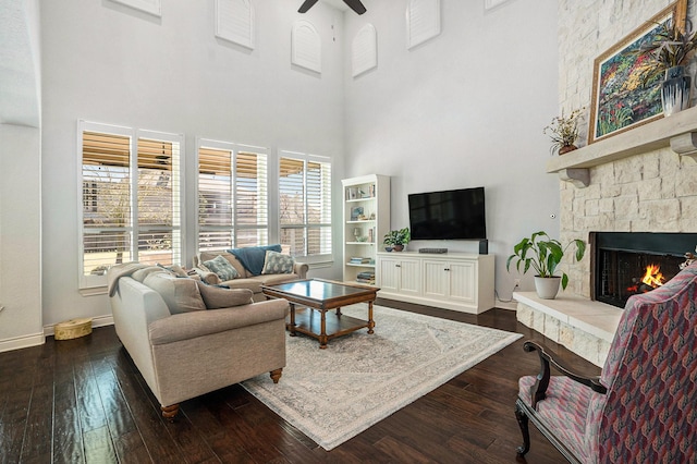 living area with a healthy amount of sunlight, a fireplace, ceiling fan, and dark wood-style flooring