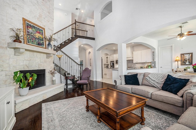 living room with wood finished floors, visible vents, ceiling fan, stairs, and a stone fireplace