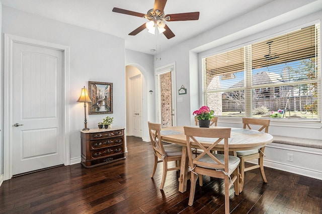 dining space featuring arched walkways, baseboards, ceiling fan, and dark wood-style flooring