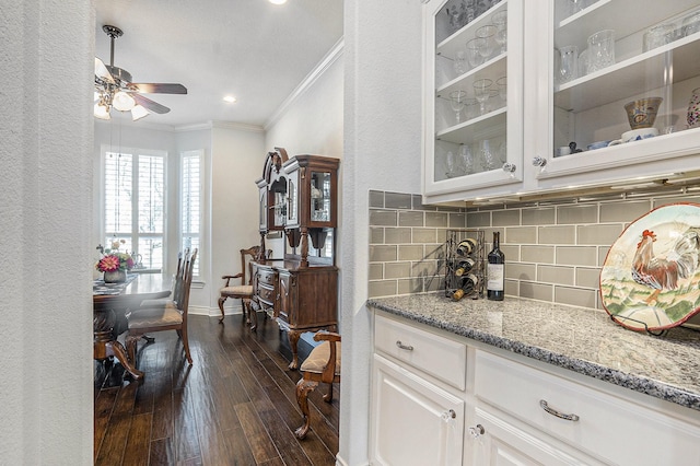 bar featuring dark wood-type flooring, ornamental molding, a ceiling fan, backsplash, and baseboards