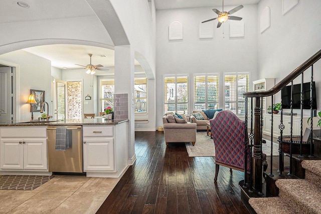 kitchen featuring ceiling fan, open floor plan, dark stone countertops, arched walkways, and stainless steel dishwasher