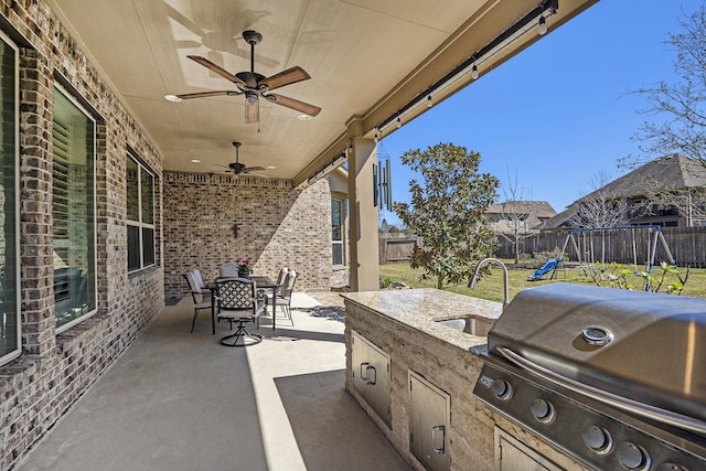 view of patio with a sink, a fenced backyard, a playground, a grill, and an outdoor kitchen