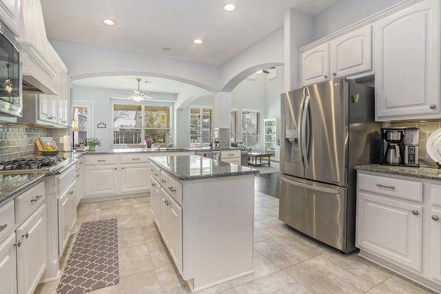 kitchen featuring a ceiling fan, backsplash, a kitchen island, arched walkways, and appliances with stainless steel finishes