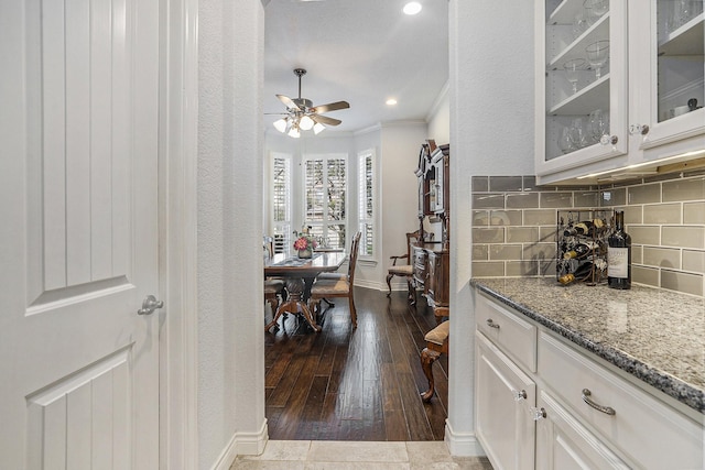 kitchen featuring glass insert cabinets, baseboards, crown molding, ceiling fan, and decorative backsplash