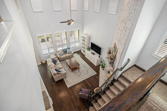 living room featuring baseboards, stairs, a high ceiling, wood finished floors, and a ceiling fan