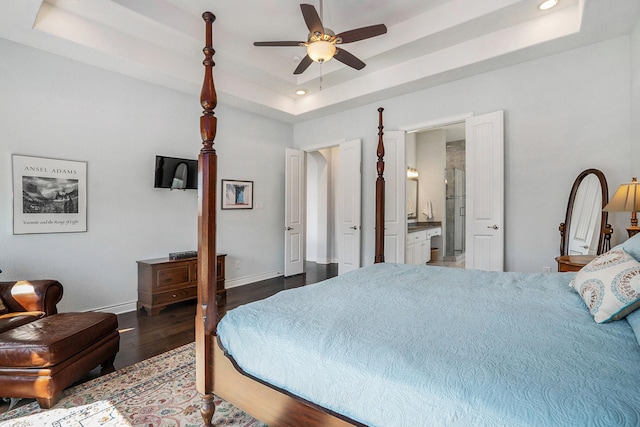 bedroom with connected bathroom, baseboards, a tray ceiling, recessed lighting, and wood finished floors