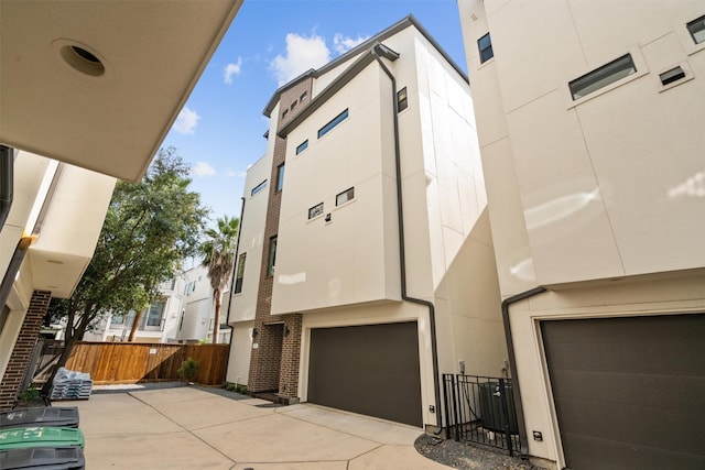 view of front of house with fence, concrete driveway, central AC unit, stucco siding, and an attached garage