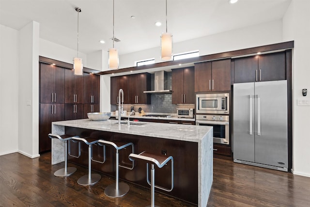 kitchen featuring dark wood-type flooring, wall chimney range hood, dark brown cabinets, and stainless steel appliances