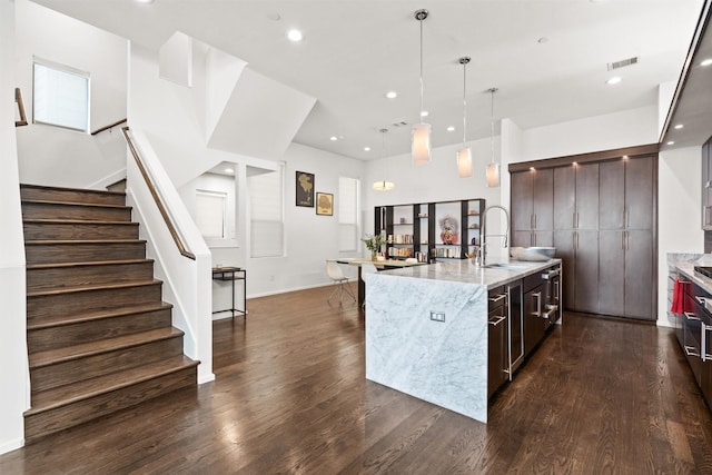 kitchen with an island with sink, dark wood-style flooring, a sink, hanging light fixtures, and dark brown cabinets