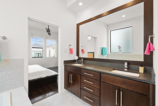 ensuite bathroom with a sink, marble finish floor, recessed lighting, and double vanity