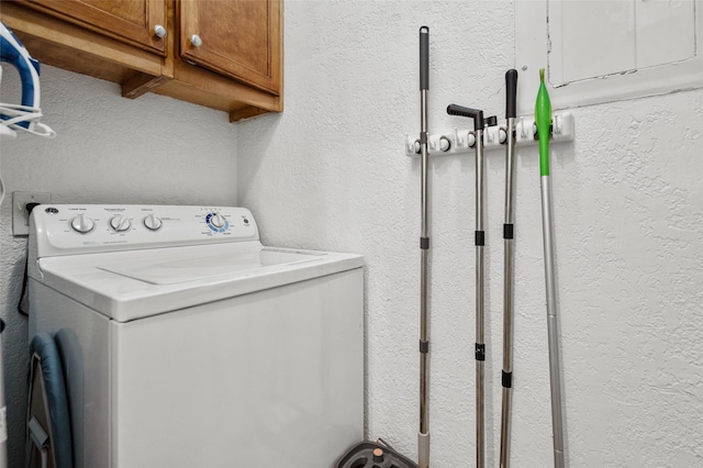 clothes washing area with cabinet space, washer / dryer, and a textured wall