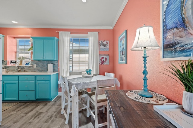 dining space with light wood-style flooring, crown molding, and a textured wall