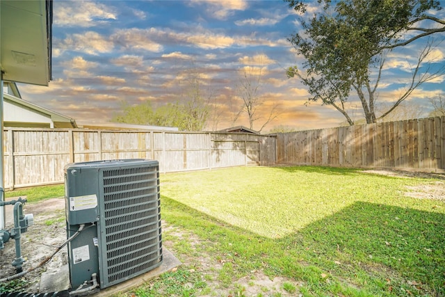 yard at dusk featuring a fenced backyard and central AC