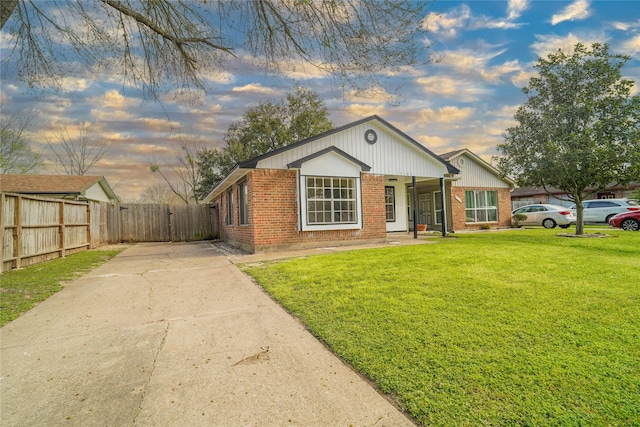 view of front facade featuring brick siding, concrete driveway, a lawn, and fence