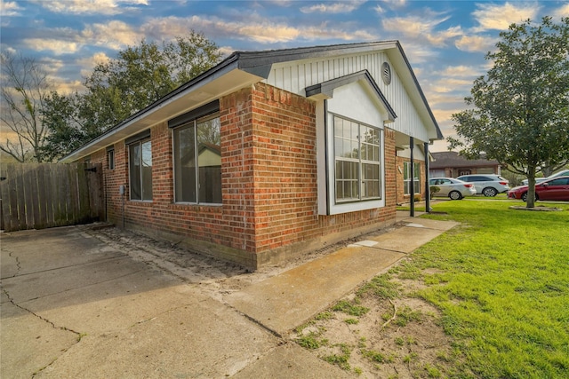 property exterior at dusk with brick siding, a lawn, and fence