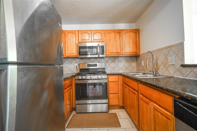 kitchen with light tile patterned floors, a sink, stainless steel appliances, a textured ceiling, and dark countertops