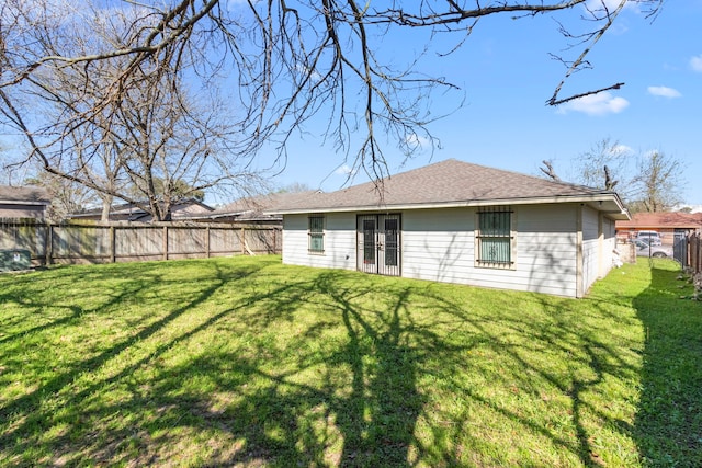 rear view of property with a yard, a fenced backyard, and a shingled roof