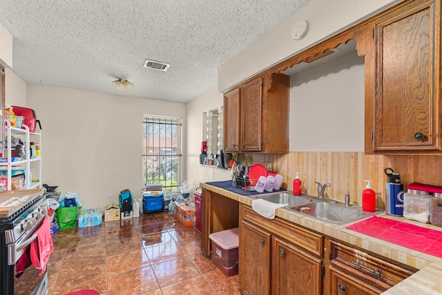 kitchen with visible vents, light countertops, brown cabinets, stainless steel range with electric stovetop, and a sink