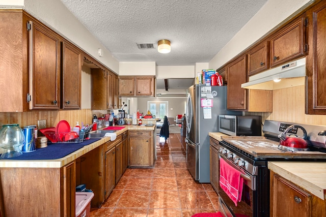 kitchen with a peninsula, stainless steel appliances, light countertops, under cabinet range hood, and brown cabinets