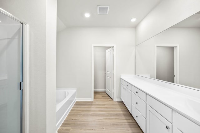 bathroom with visible vents, a shower stall, wood finished floors, a bath, and vanity