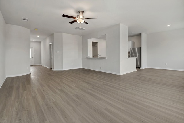 unfurnished living room featuring visible vents, baseboards, a ceiling fan, and wood finished floors