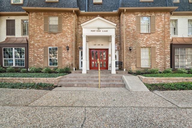 property entrance featuring brick siding, mansard roof, and roof with shingles