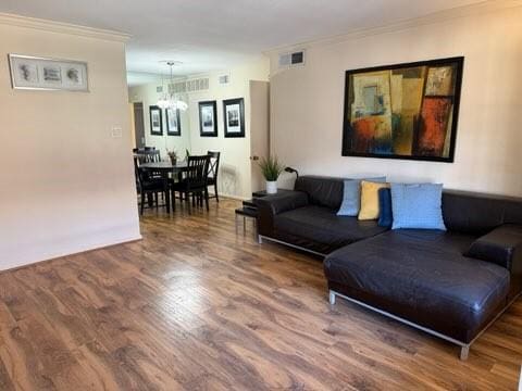 living room featuring visible vents, wood finished floors, a chandelier, and crown molding