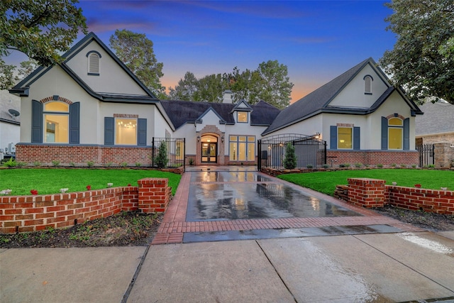 view of front of home featuring brick siding, stucco siding, a yard, driveway, and a gate