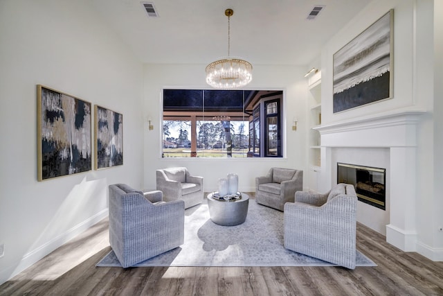 living room featuring built in shelves, wood finished floors, visible vents, a glass covered fireplace, and a notable chandelier