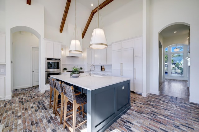 kitchen featuring high vaulted ceiling, light countertops, stainless steel double oven, white cabinetry, and a sink