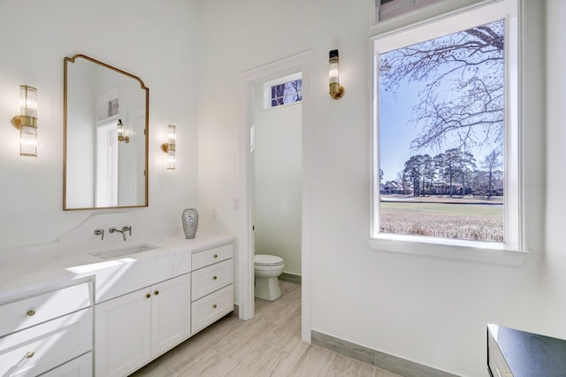 bathroom with a wealth of natural light, baseboards, toilet, and vanity