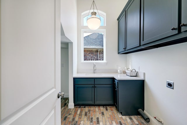 laundry area with electric dryer hookup, a sink, cabinet space, brick floor, and baseboards