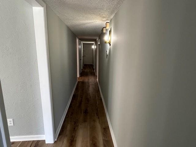 hall featuring dark wood finished floors, a textured ceiling, and baseboards