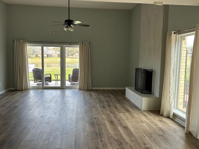 unfurnished living room featuring a wealth of natural light, baseboards, a ceiling fan, and wood finished floors